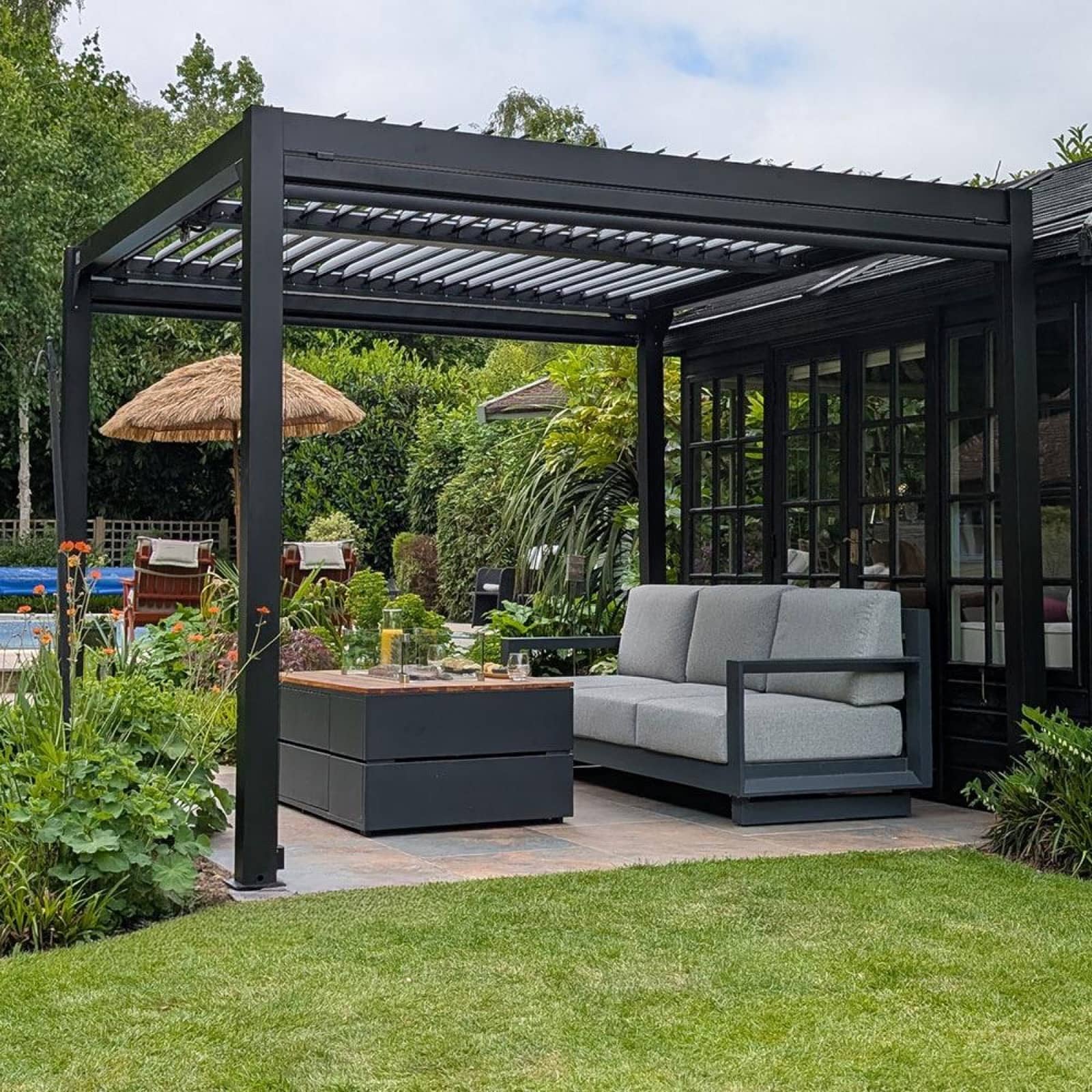 Compact black aluminium pergola arranged over a garden seating area