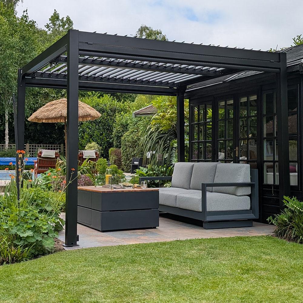 Fire table and lounge seating under a pergola beside a garden pool