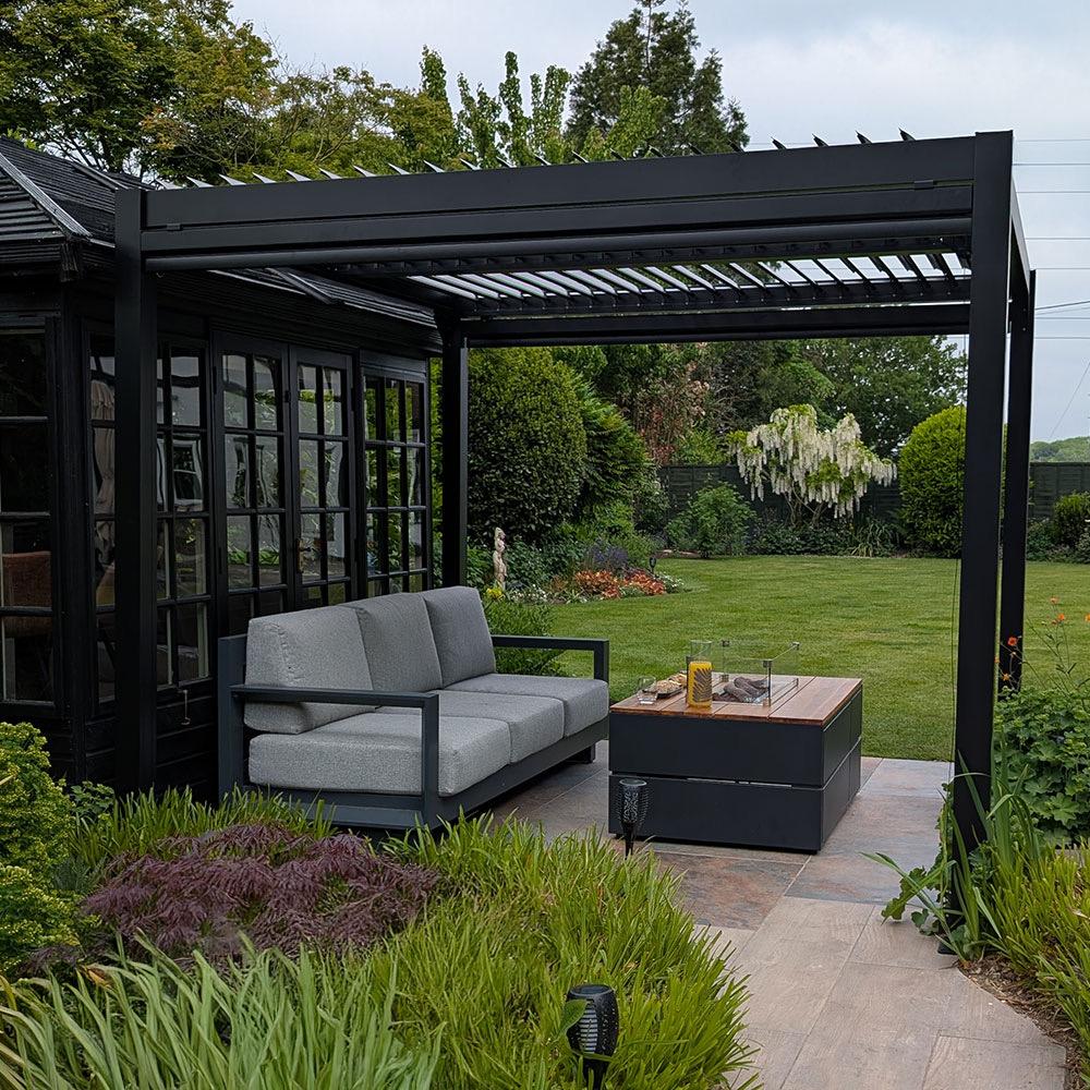 Fire table beside outdoor sofa seating under a louvred pergola in a garden setting